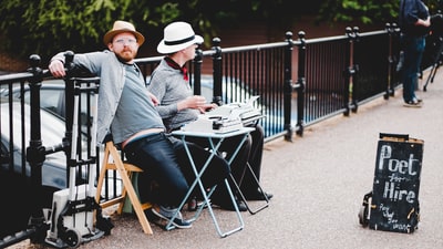 两名男子坐在长凳上，白天靠在招牌旁的金属栏杆上